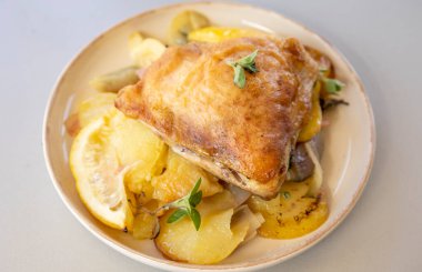 Kızarmış tavuk budu, patates, limon ve soğan ile yakın plan bir tabakta.