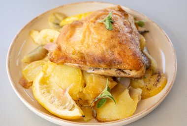 Kızarmış tavuk budu, patates, limon ve soğan ile yakın plan bir tabakta.