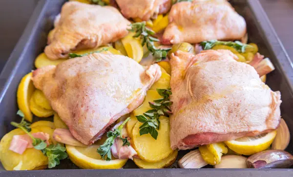  Çiğ tavuk budu, patates, limon ve soğan tablasında yakın plan pişirmeye hazır.