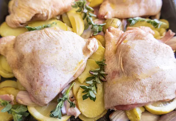  Çiğ tavuk budu, patates, limon ve soğan tablasında yakın plan pişirmeye hazır.