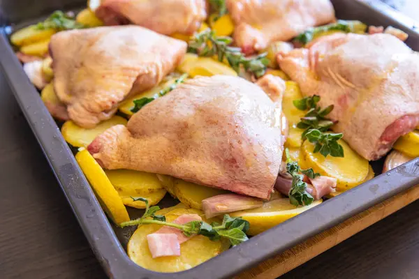  Çiğ tavuk budu, patates, limon ve soğan tablasında yakın plan pişirmeye hazır.