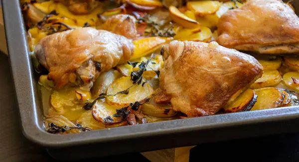 Patates, limon ve soğanlı kızarmış tavuk budu yakın plan bir tepside.