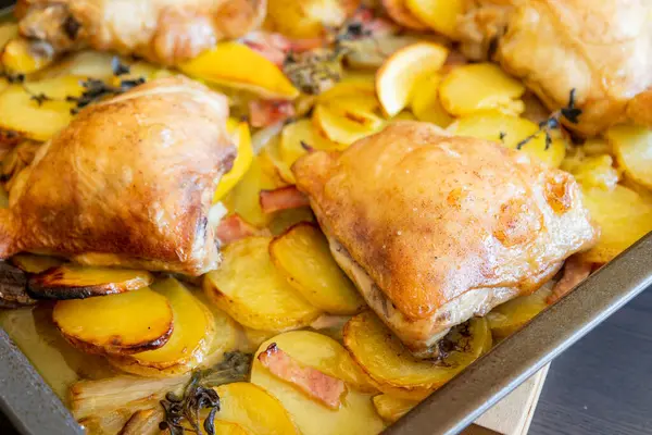 Patates, limon ve soğanlı kızarmış tavuk budu yakın plan bir tepside.