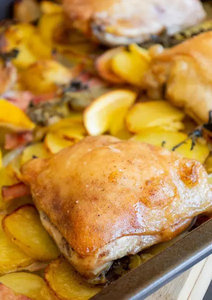 Patates, limon ve soğanlı kızarmış tavuk budu yakın plan bir tepside.