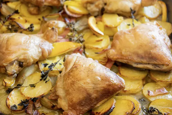 Patates, limon ve soğanlı kızarmış tavuk budu yakın plan bir tepside.