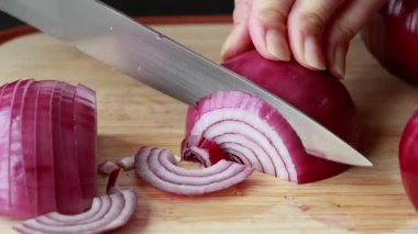 Ahşap kesim tahtasına kırmızı soğan dilimleyen kadın.