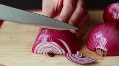 Ahşap kesim tahtasına kırmızı soğan dilimleyen kadın.