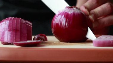 Ahşap kesim tahtasına kırmızı soğan dilimleyen kadın.