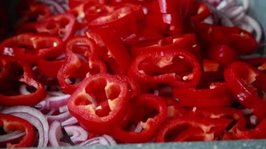  Dilimlenmiş kırmızı soğanlar ve dilimlenmiş kırmızı dolma biberler yakın bir tepside dizilmiş.