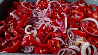  Dilimlenmiş kırmızı soğanlar ve dilimlenmiş kırmızı dolma biberler yakın bir tepside dizilmiş.