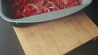  Dilimlenmiş kırmızı soğanlar ve dilimlenmiş kırmızı dolma biberler yakın bir tepside dizilmiş.