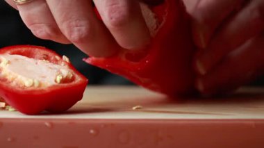 Kadınların elleri, tahta kesme tahtasında kırmızı bir dolma biberi temizler ve doğrar.