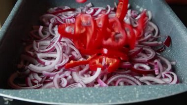  Dilimlenmiş kırmızı soğanlar ve dilimlenmiş kırmızı dolma biberler yakın bir tepside dizilmiş.