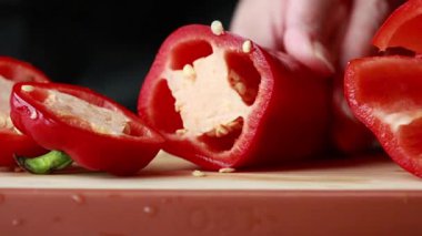 Kadınların elleri, tahta kesme tahtasında kırmızı bir dolma biberi temizler ve doğrar.