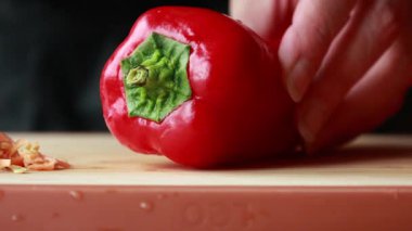 Kadınların elleri, tahta kesme tahtasında kırmızı bir dolma biberi temizler ve doğrar.