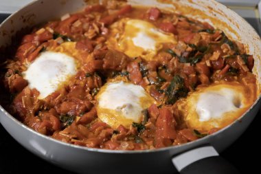 Taze pişmiş Shakshuka 'nın yakın çekimi, tavada servis edilen bol domates soslu haşlanmış yumurtalarla lezzetli bir yemek. Nefis bir kahvaltı için mükemmel..