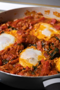 Taze pişmiş Shakshuka 'nın yakın çekimi, tavada servis edilen bol domates soslu haşlanmış yumurtalarla lezzetli bir yemek. Nefis bir kahvaltı için mükemmel..