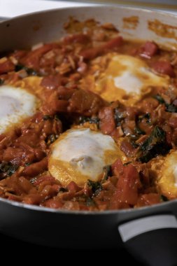 Taze pişmiş Shakshuka 'nın yakın çekimi, tavada servis edilen bol domates soslu haşlanmış yumurtalarla lezzetli bir yemek. Nefis bir kahvaltı için mükemmel..