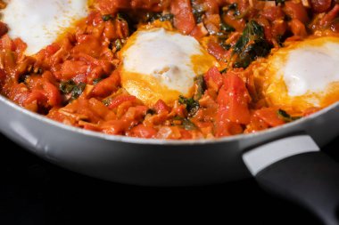 Taze pişmiş Shakshuka 'nın yakın çekimi, tavada servis edilen bol domates soslu haşlanmış yumurtalarla lezzetli bir yemek. Nefis bir kahvaltı için mükemmel..