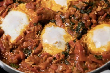 Taze pişmiş Shakshuka 'nın yakın çekimi, tavada servis edilen bol domates soslu haşlanmış yumurtalarla lezzetli bir yemek. Nefis bir kahvaltı için mükemmel..