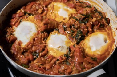 Taze pişmiş Shakshuka 'nın yakın çekimi, tavada servis edilen bol domates soslu haşlanmış yumurtalarla lezzetli bir yemek. Nefis bir kahvaltı için mükemmel..