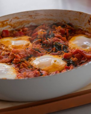 Taze pişmiş Shakshuka 'nın yakın çekimi, tavada servis edilen bol domates soslu haşlanmış yumurtalarla lezzetli bir yemek. Nefis bir kahvaltı için mükemmel..