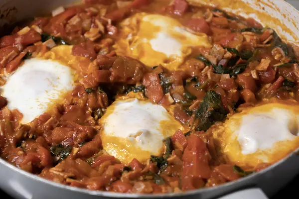 Taze pişmiş Shakshuka 'nın yakın çekimi, tavada servis edilen bol domates soslu haşlanmış yumurtalarla lezzetli bir yemek. Nefis bir kahvaltı için mükemmel..