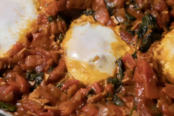 Taze pişmiş Shakshuka 'nın yakın çekimi, tavada servis edilen bol domates soslu haşlanmış yumurtalarla lezzetli bir yemek. Nefis bir kahvaltı için mükemmel..