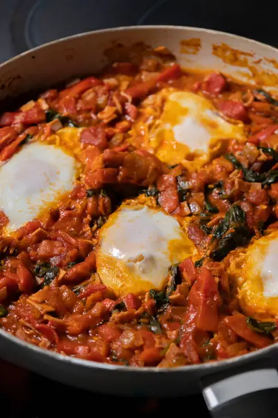 Taze pişmiş Shakshuka 'nın yakın çekimi, tavada servis edilen bol domates soslu haşlanmış yumurtalarla lezzetli bir yemek. Nefis bir kahvaltı için mükemmel..