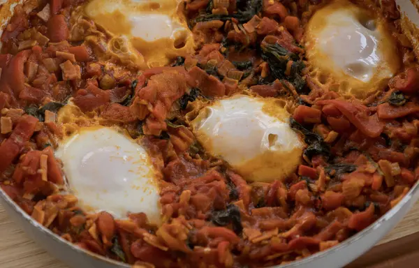 Taze pişmiş Shakshuka 'nın yakın çekimi, tavada servis edilen bol domates soslu haşlanmış yumurtalarla lezzetli bir yemek. Nefis bir kahvaltı için mükemmel..