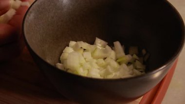 Kadın elleri ahşap kesim tahtasına sarı soğan dilimliyor.