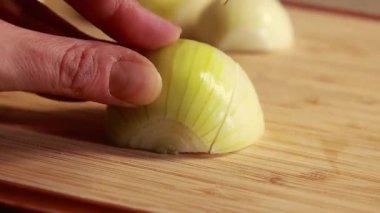 Kadın elleri ahşap kesim tahtasına sarı soğan dilimliyor.
