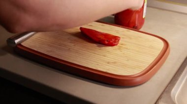 Kadın elleri, konserve kırmızı dolma biberi dilimliyor. Ahşap kesim tahtasına yakın plan.