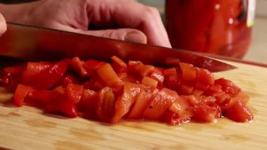 Kadın elleri, konserve kırmızı dolma biberi dilimliyor. Ahşap kesim tahtasına yakın plan.
