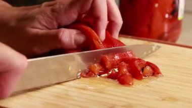 Kadın elleri, konserve kırmızı dolma biberi dilimliyor. Ahşap kesim tahtasına yakın plan.