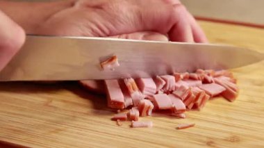 Kadın elleri ahşap kesim tahtasında jambon dilimliyor.