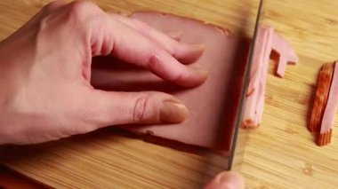Kadın elleri ahşap kesim tahtasında jambon dilimliyor.