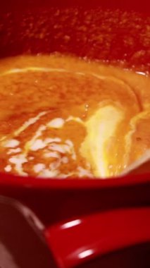 Kırmızı bir tencerede kaynayan kremalı havuç çorbası. Pürüzsüz, canlı doku ve zengin renk. 