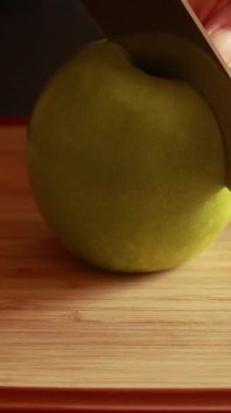 Tahta kesme tahtasının üzerinde taze yeşil bir elmayı kesen bir kadının ellerini yakın plan çek.