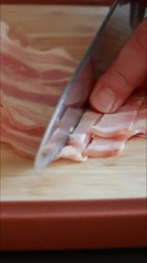 Bir kadının elleri kesme tahtasında çiğ domuz pastırması dilimlerken.