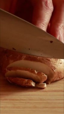 Bir kadının ellerini dikkatlice kesme tahtasındaki taze mantarları keserken yakın plan.