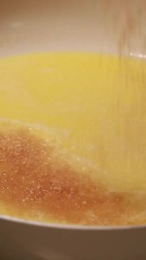 Tereyağı ve şekerin yakın çekimi beyaz bir tavada eriyor.