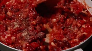 Domatesler ve fasulyeler tavada pişiyor, zengin bir sosta yavaşça kaynıyor.