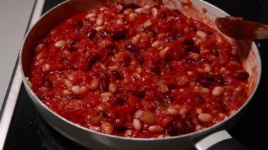 Domatesler ve fasulyeler tavada pişiyor, zengin bir sosta yavaşça kaynıyor.