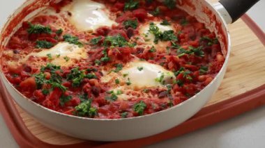 Sıcak, lezzetli bir Shakshuka 'nın yakın çekim videosu. Yumurta ve fasulye, zengin bir domates sosunda kaynıyor.