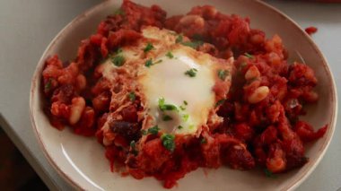 Sıcak, lezzetli bir Shakshuka 'nın yakın çekim videosu. Yumurta ve fasulye, zengin bir domates sosunda kaynıyor.
