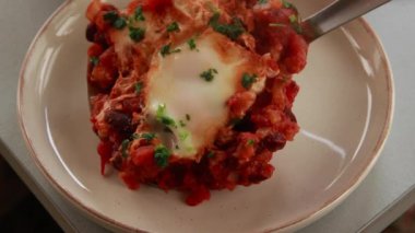 Sıcak, lezzetli bir Shakshuka 'nın yakın çekim videosu. Yumurta ve fasulye, zengin bir domates sosunda kaynıyor.