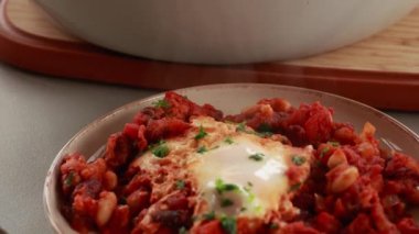 Sıcak, lezzetli bir Shakshuka 'nın yakın çekim videosu. Yumurta ve fasulye, zengin bir domates sosunda kaynıyor.