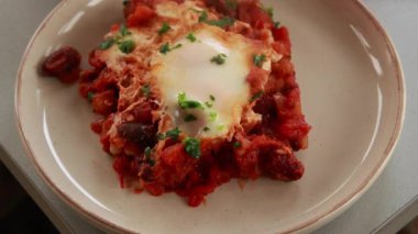Sıcak, lezzetli bir Shakshuka 'nın yakın çekim videosu. Yumurta ve fasulye, zengin bir domates sosunda kaynıyor.