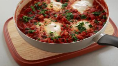 Sıcak, lezzetli bir Shakshuka 'nın yakın çekim videosu. Yumurta ve fasulye, zengin bir domates sosunda kaynıyor.
